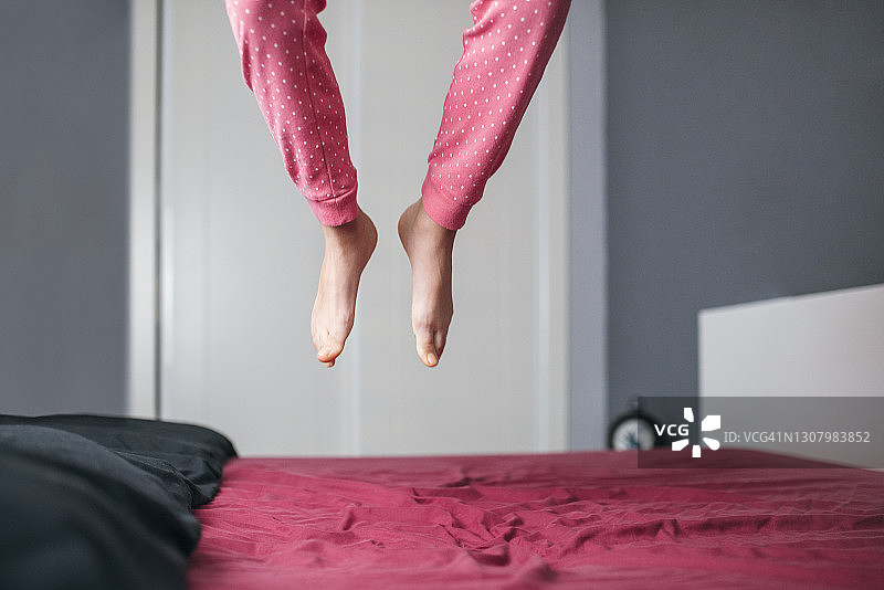 小女孩在父母床上跳跃玩耍的正面照，生活方式概念图片素材