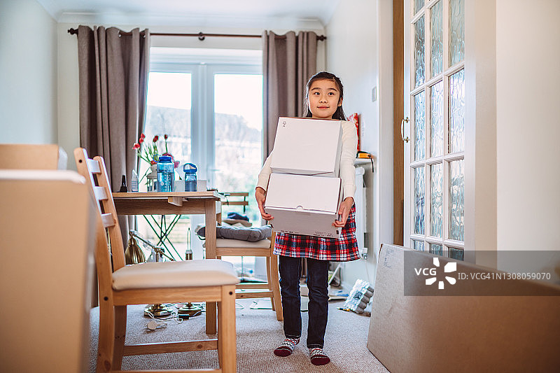 在搬进新家时，快乐的女孩帮忙搬运新家电的箱子图片素材