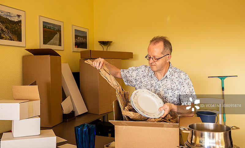 独自一人在空荡荡的公寓里搬家，将东西装在纸板箱里，看着怀旧物品的老年男人图片素材