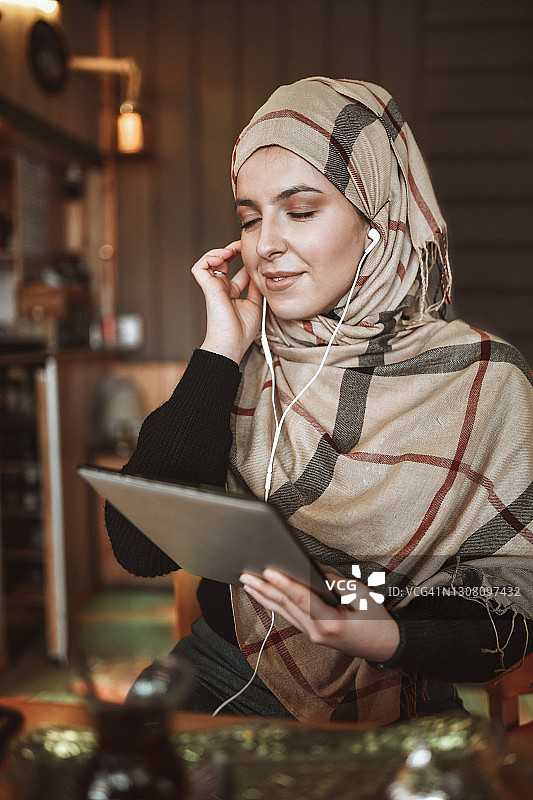 戴着头巾用平板电脑听歌的平静现代穆斯林女性图片素材