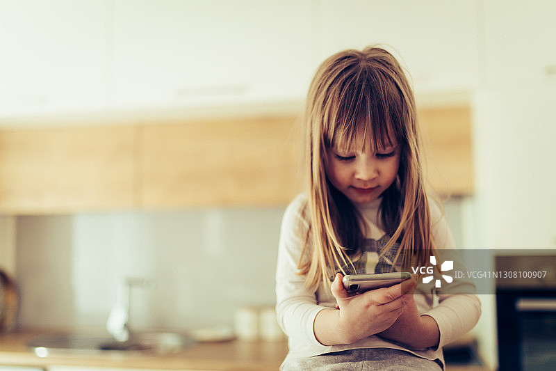 可爱的女婴在家使用智能手机图片素材
