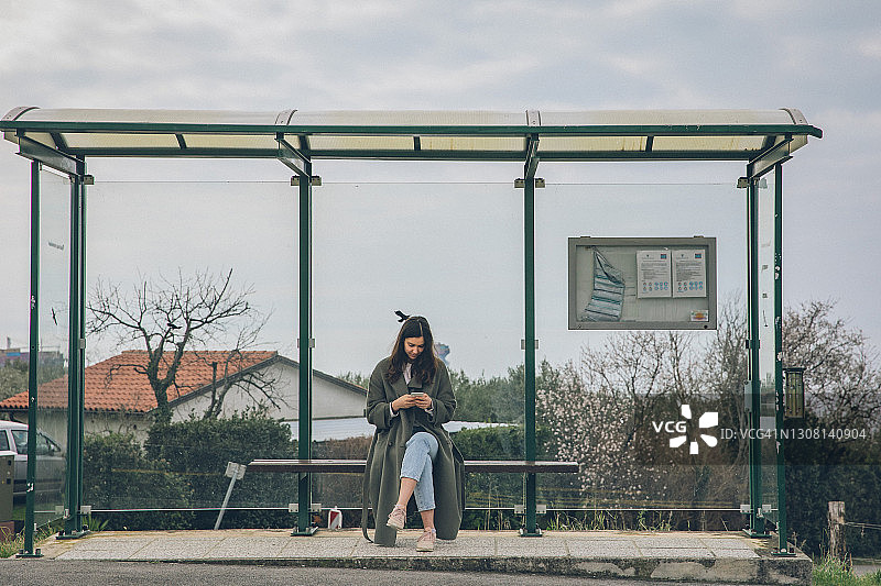 年轻女人在巴士站使用智能手机图片素材