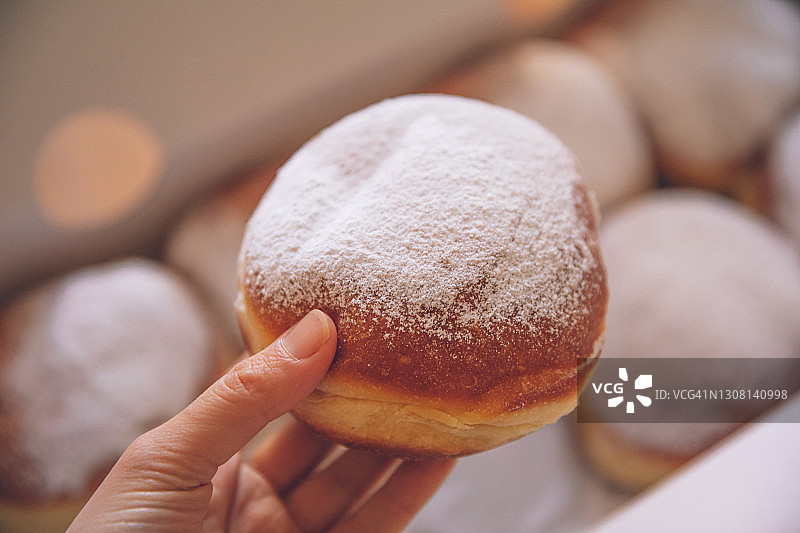 手持裹满糖粉的新鲜甜甜圈图片素材