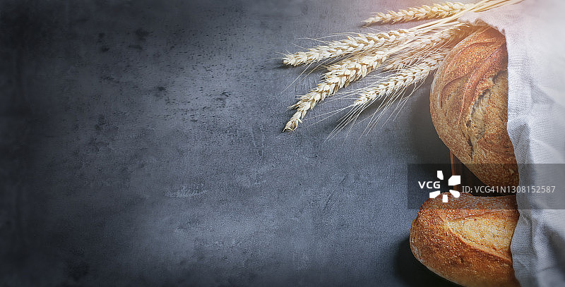 深色台面上两个新鲜的自制面包，麦穗营造氛围，留有文字空间图片素材