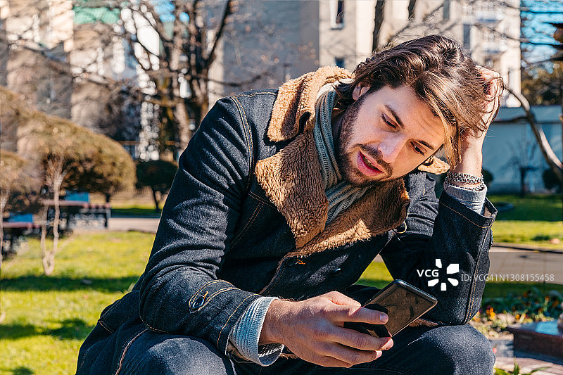 坐在城市公园里使用手机的年轻男子面部表情图片素材
