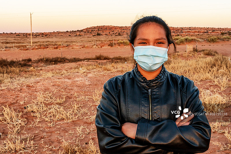 纪念碑谷犹他州，一位微笑的纳瓦霍族美国原住民年轻女子特写，她戴着口罩，双臂交叉在她家附近图片素材
