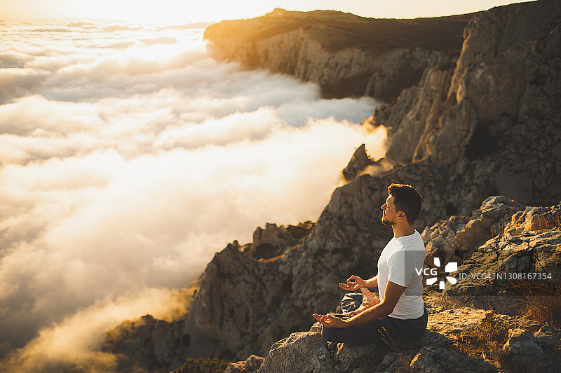 日落时分在壮丽山景中冥想的男人，独自祈祷，感受自然与精神和谐图片素材