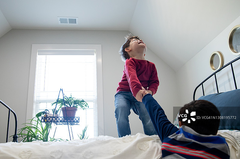 可爱的小男孩们努力将彼此抬到卧室的高床上图片素材