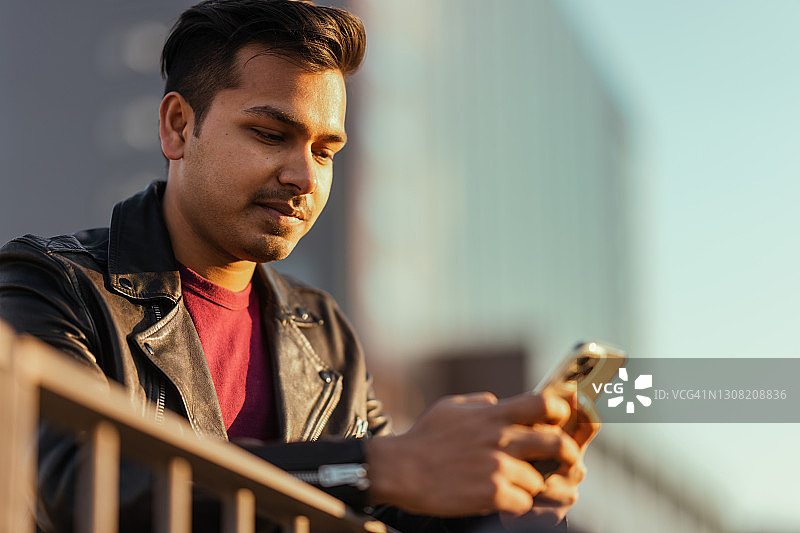 在城市里使用智能手机的年轻帅气印度男人图片素材