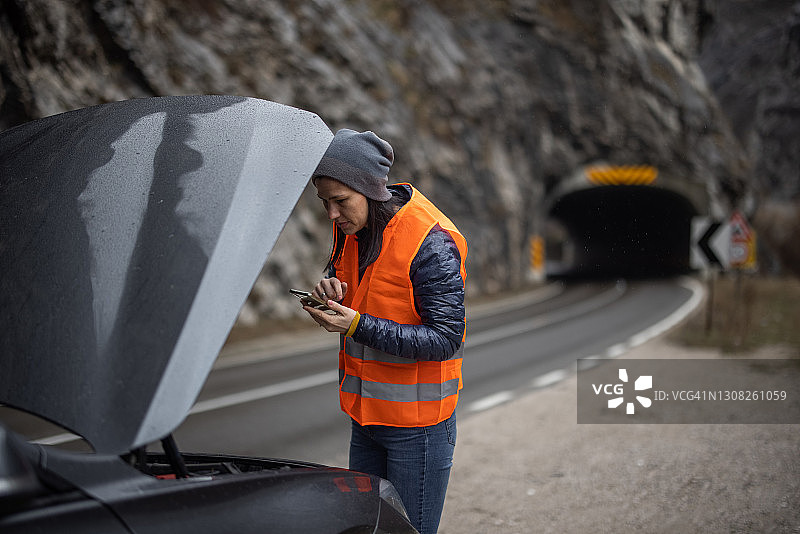 穿反光背心的女人在看汽车引擎盖并拿着手机图片素材