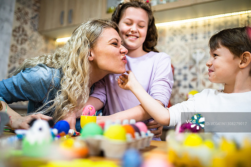 年轻的母亲和她的两个可爱的孩子在家中快乐地为复活节彩蛋涂色图片素材