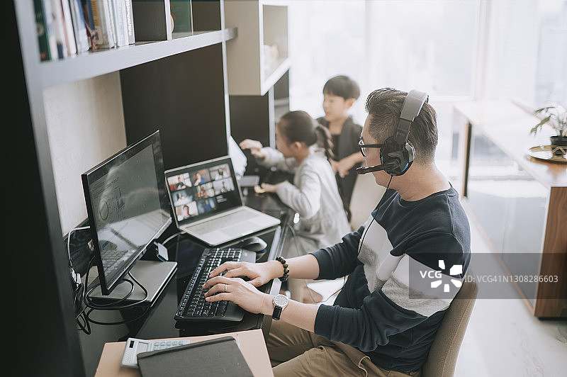 亚洲父亲在家工作，与同事进行视频通话，孩子们在他旁边使用平板电脑图片素材