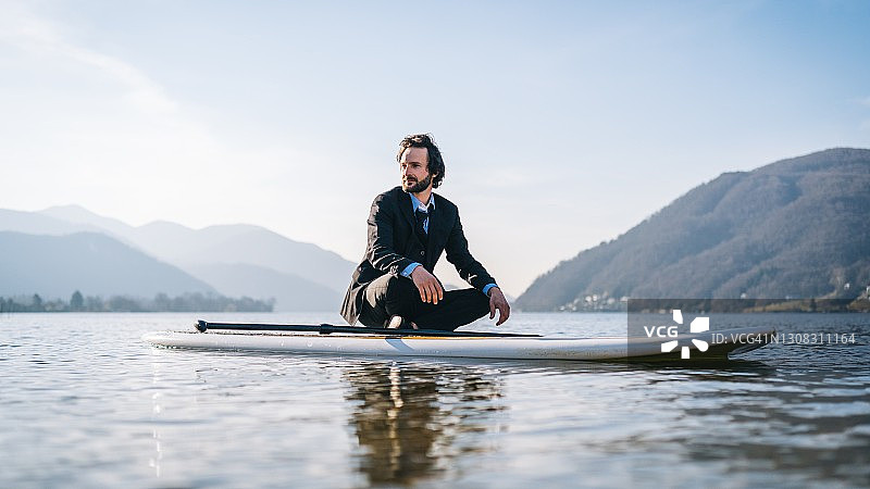 商务男士在早晨沿湖岸划桨板图片素材