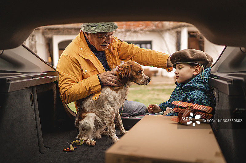 孙子和爷爷在汽车后备箱里和狗玩耍图片素材