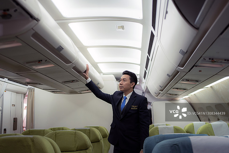 穿着制服站在飞机内乘客座位上的自信亚洲男飞行员图片素材