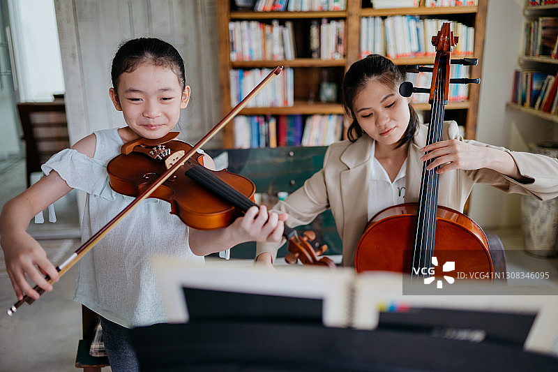 美丽的母亲在家和可爱的女儿一起演奏乐器图片素材