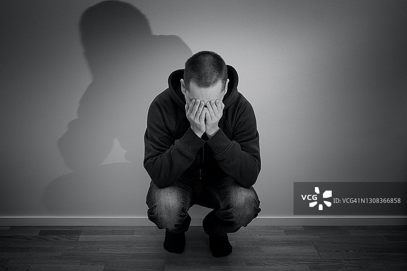 年轻的白人男子蹲着并抱着他的脸图片素材