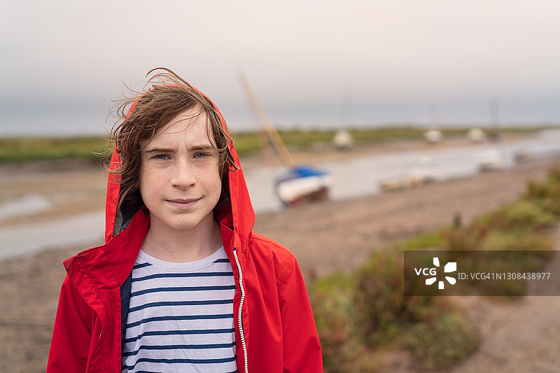 少年穿着雨衣在潮汐河边的大风天里图片素材