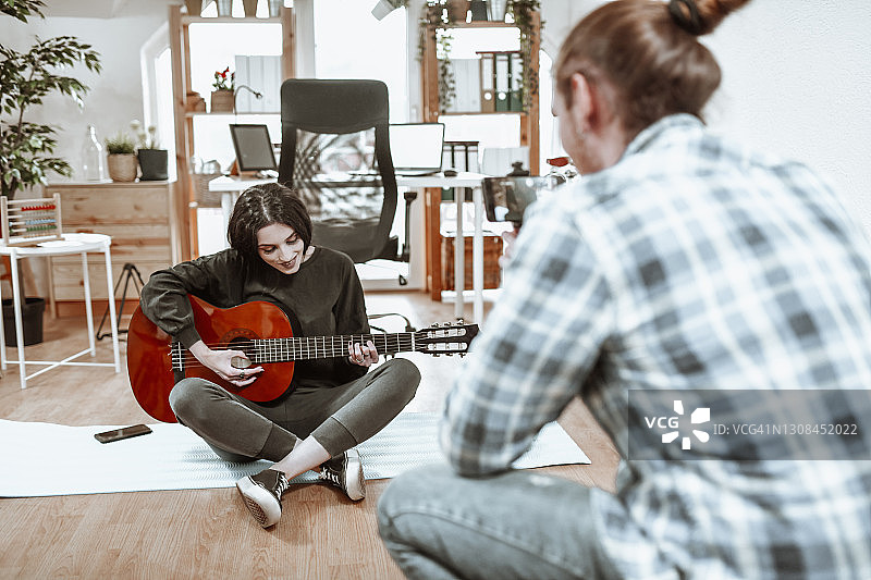 微笑女性与留长发的潮男男友一起制作吉他演奏教学视频图片素材