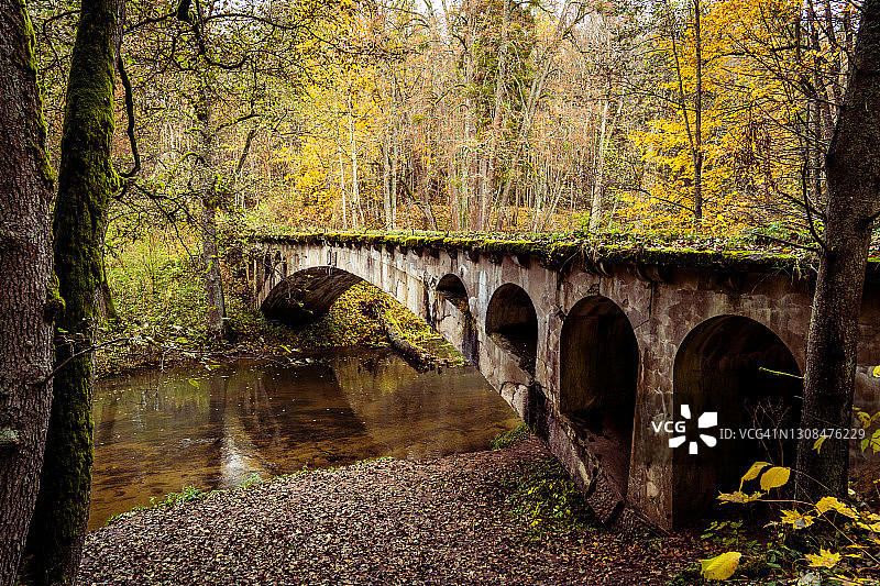 河流上的旧拱桥，周围环绕着茂密的秋季森林图片素材