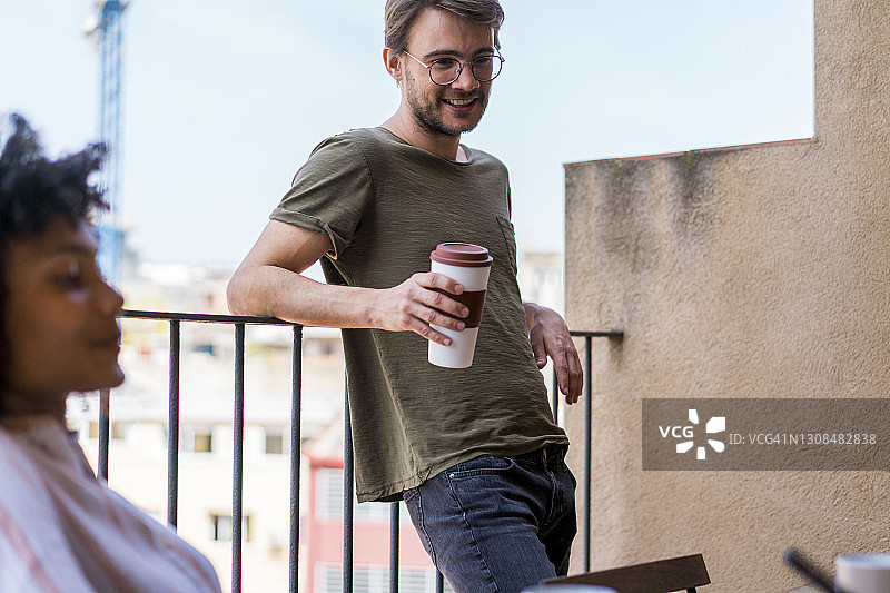 年轻男企业家在办公室咖啡休息时间手拿可重复使用杯子倚靠在栏杆上图片素材