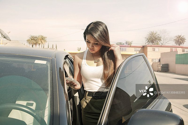 年轻女人站在城市汽车旁使用手机图片素材