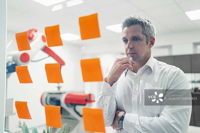 年长的工程师看着贴在工厂玻璃墙上的便利贴，思考商业计划图片素材