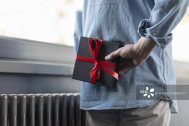 男人站在家里，手里拿着身后的礼品盒图片素材