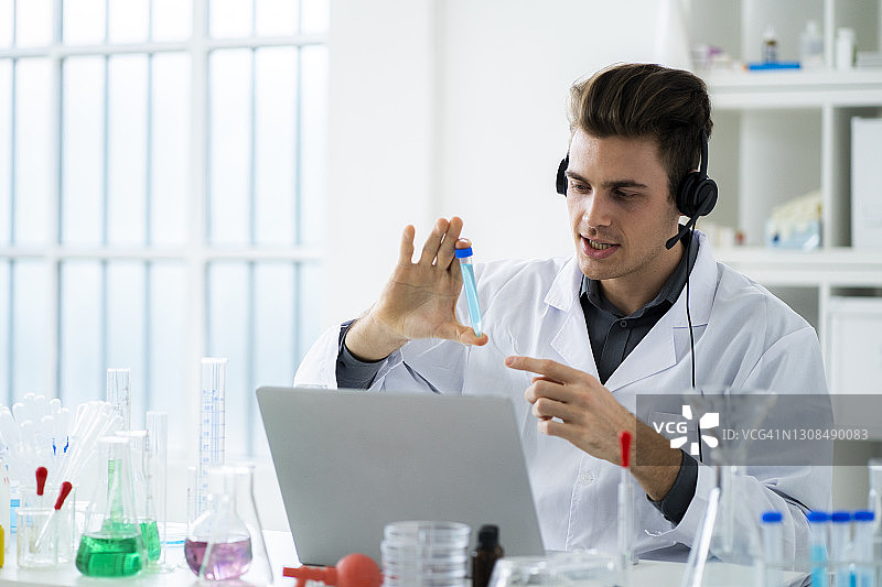 年轻男科学家在实验室里拿着试管进行视频通话图片素材