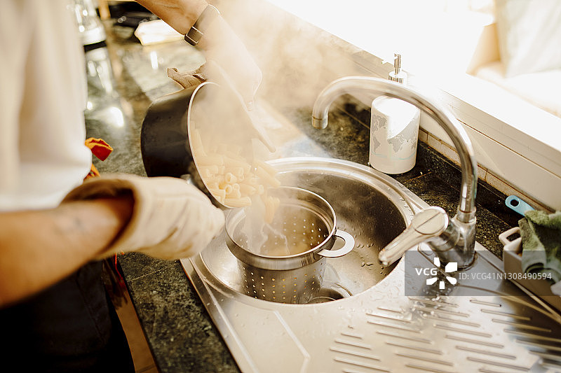 年轻男人将锅中的开水倒在滤水器中的意大利面上图片素材