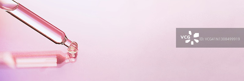 玻璃滴管将透明保湿乳液滴在粉色背景上特写图片素材