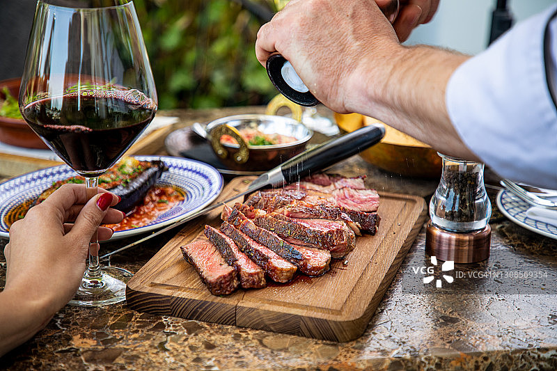 用研磨盐给三分熟牛排调味，在餐厅的木板上切割图片素材