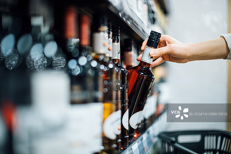女人在超市酒品区挑选瓶装酒的特写图片素材