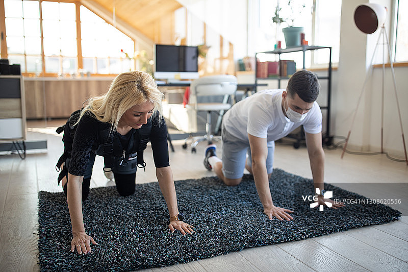 私人教练在办公室指导穿着肌肉电刺激服的女性锻炼图片素材