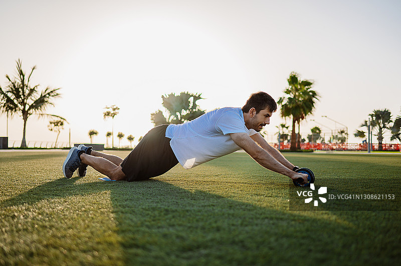 男人在户外用健腹轮锻炼腹部和核心肌肉图片素材