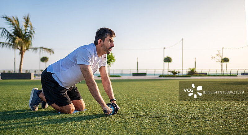 男人在户外用健腹轮锻炼腹部和核心肌肉图片素材