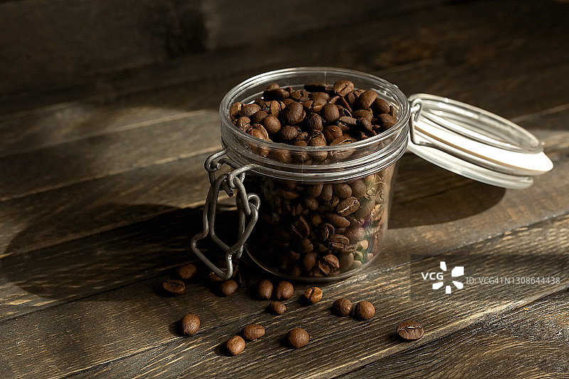 咖啡豆倒入玻璃罐中，棕色木质背景图片素材