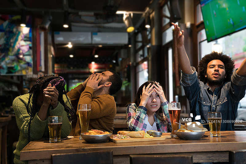 一群沮丧的朋友在酒吧观看足球比赛，喝啤酒和吃零食图片素材
