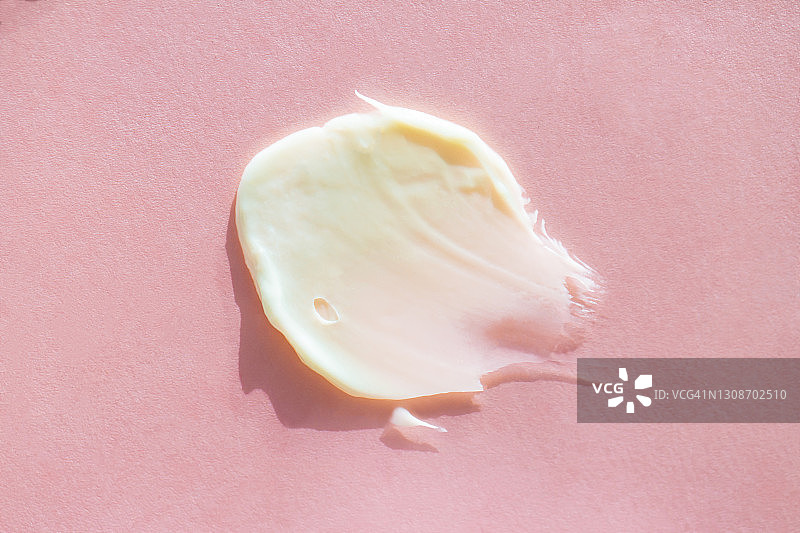 浅粉色背景上米色身体霜涂抹，天然护肤化妆品概念，极致特写扁平风格图片素材