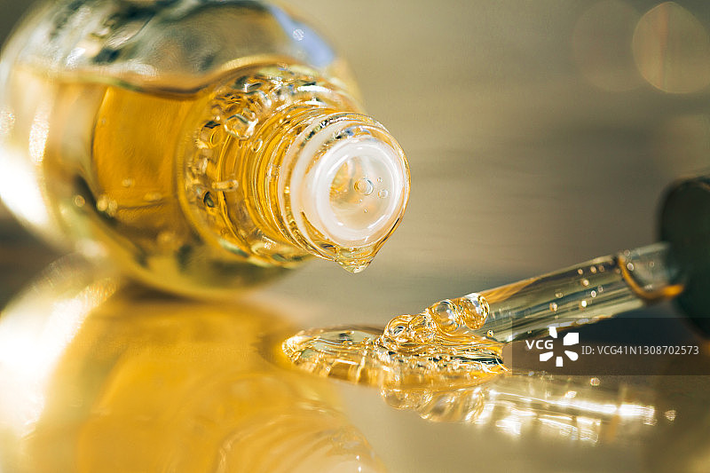 从玻璃瓶和滴管滴在灰色表面上的明黄色精油滴图片素材