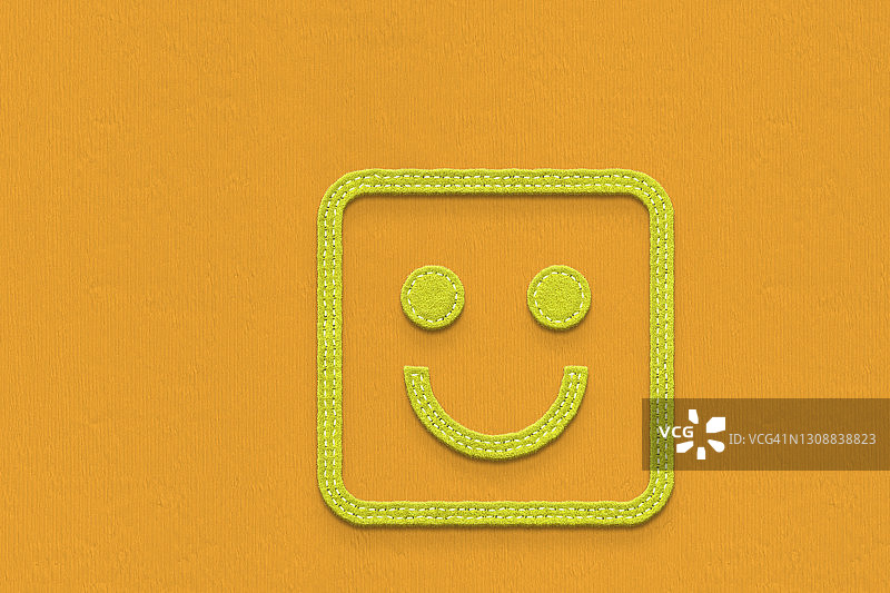 橙色背景中绿色毛毡制成的快乐方形笑脸图片素材