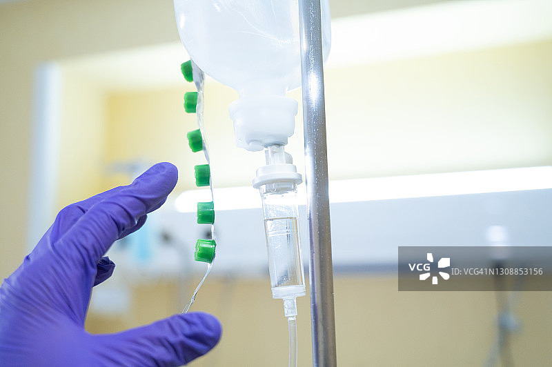 戴着防护手套的人准备取下挂在医院病房里的滴瓶图片素材