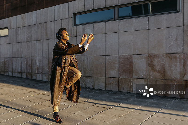 戴无线耳机在建筑物前听音乐跳舞的男人图片素材