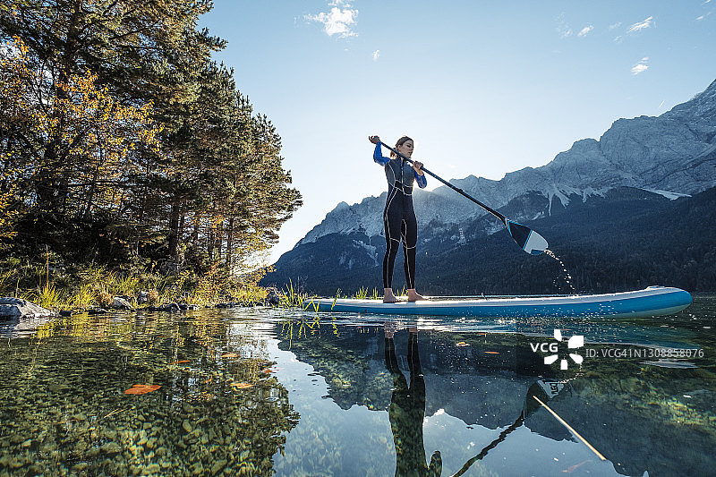 德国巴伐利亚加米施-帕滕基兴：年轻女子在艾布湖上玩桨板图片素材