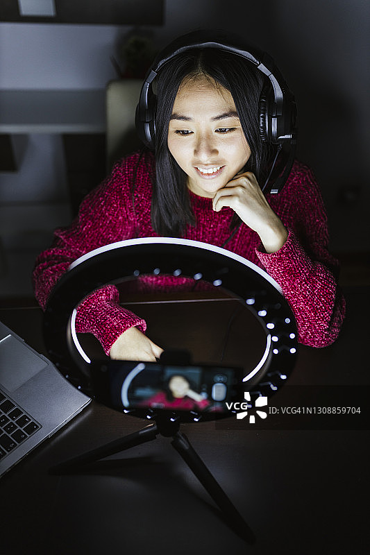 在环形灯前戴着耳机微笑的女网红图片素材