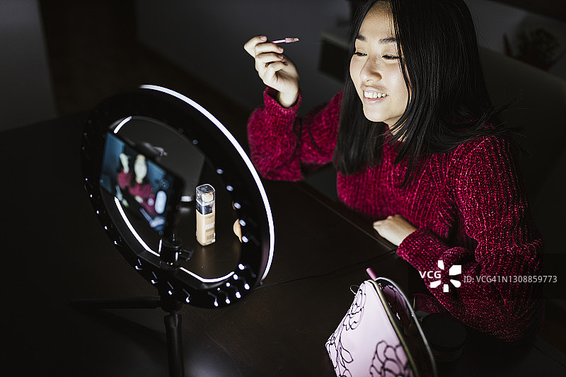 年轻女性网红在暗房拍摄视频时涂唇彩图片素材