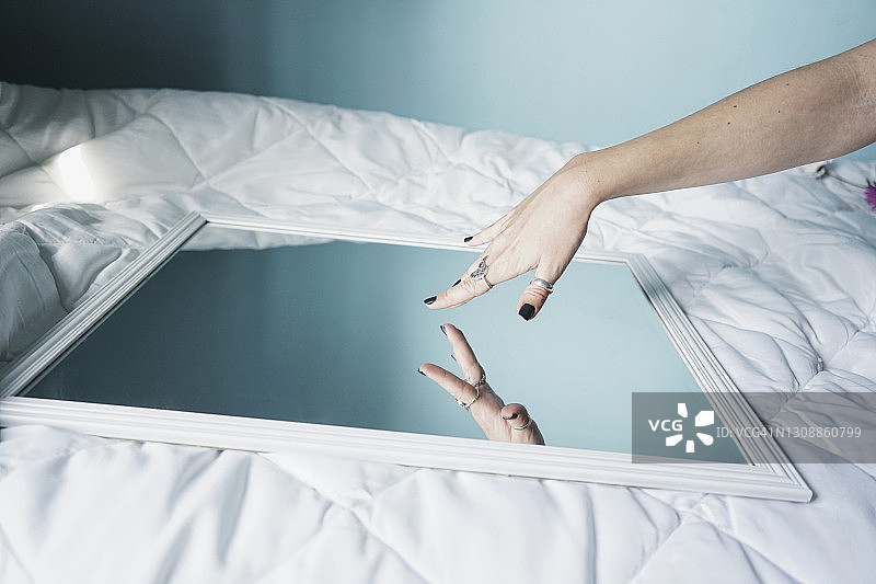 年轻女子触摸放在白色羽绒被上的镜子图片素材