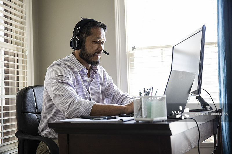 在家居办公室里戴着耳机用笔记本电脑工作的男人图片素材