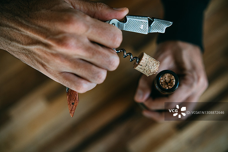 男子用开瓶器打开葡萄酒瓶，以及断裂的葡萄酒瓶塞的特写图片素材