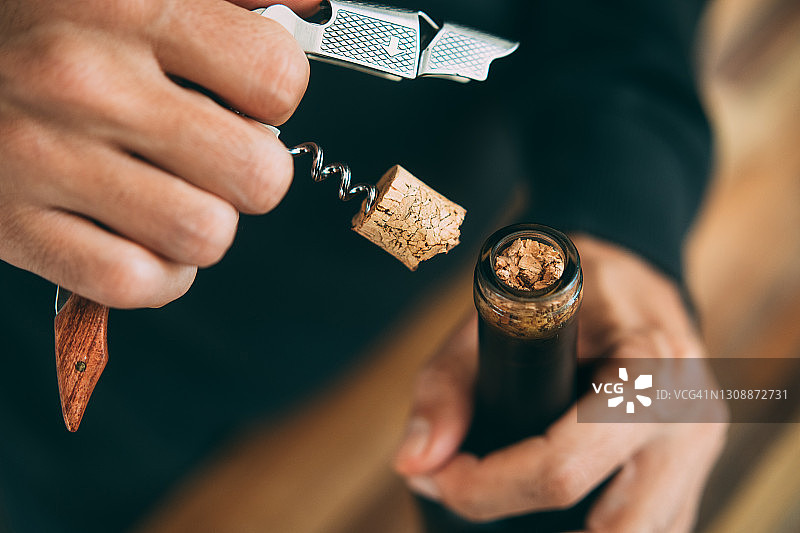 男子用开瓶器打开葡萄酒瓶，以及断裂的葡萄酒瓶塞的特写图片素材